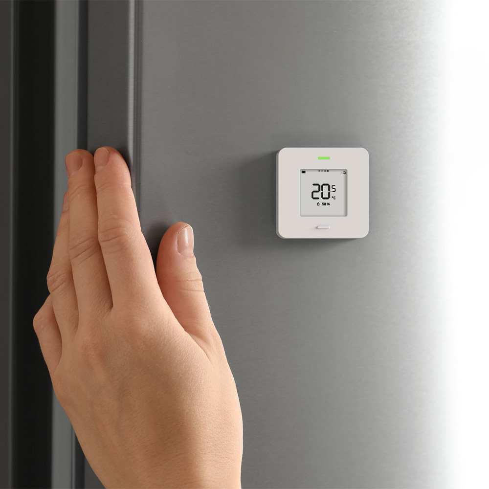 Weißer, quadratischer myStrom WiFi Button Max mit Taste, Display und LED-Leuchte an einer Wand befestigt, daneben eine Hand