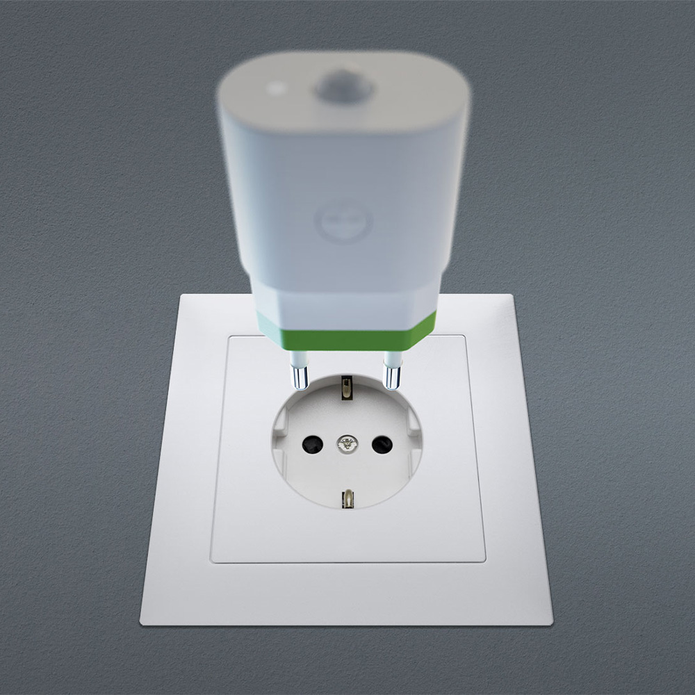 Weiß-grüner myStrom WiFi Motion Sensor kurz vor dem Einstecken in eine weiße Wandsteckdose